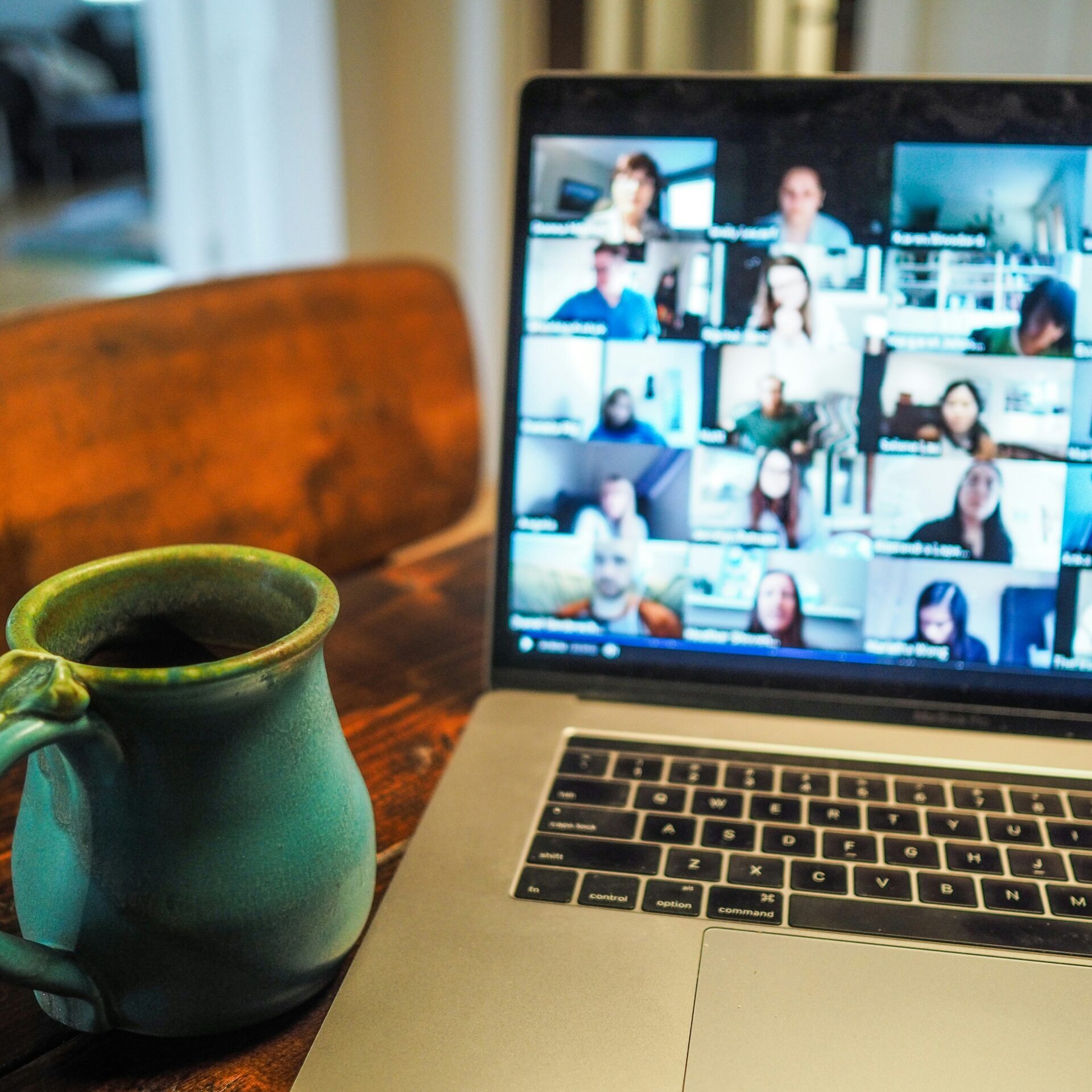 Laptop displaying a grid of people on a webinar with a green coffee cup beside on a small table
